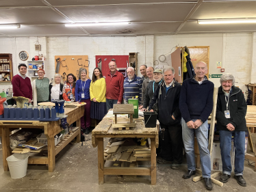 Huw stood with members of Bexhill Men's Shed around workbenches and tools